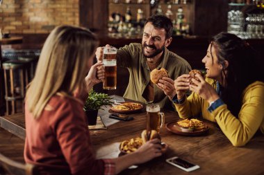 Young happy man toasting with friends while having lunch in a pub.