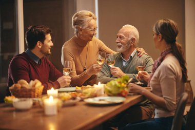 Happy mature couple celebrating and toasting with wine while having dinner with their adult children at dining table. 