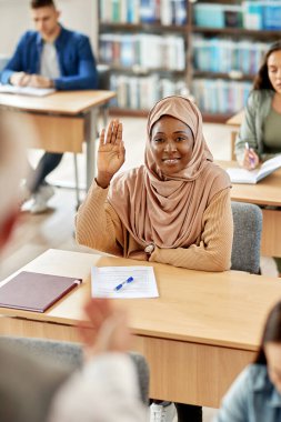 Happy Muslim student raising her arm to ask a question during a class at the university. 