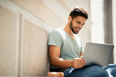 Happy student surfing the net on laptop in a hallway at the university. Copy space.