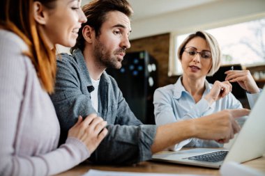 Low angle view of young couple and their real estate agent using laptop while having a meeting at home. Focus is on man. 