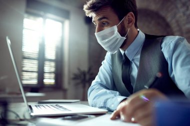 Young businessman wearing face mask while using laptop and working in the office during virus epidemic. 