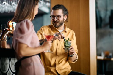 Young couple enjoying while communicating and drinking cocktails at bar counter. Focus is on man. 