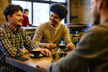 Multiracial group of young happy men drinking coffee and talking in a cafe. Focus is on Lebanese man.