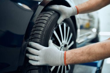 Close-up of repairman changing car tire at auto service workshop. 