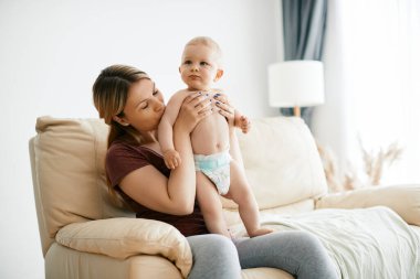Loving mother kissing baby son's arm while dressing him up at home.
