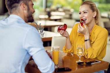 Happy couple enjoying while eating dessert and communicating in a cafe. Focus is on woman eating donuts. 