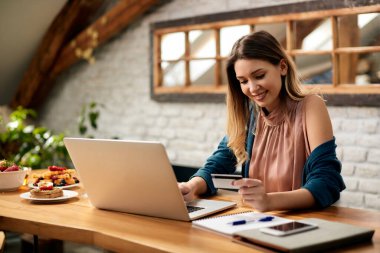 Young happy woman using credit card and laptop while shopping on the internet at home.