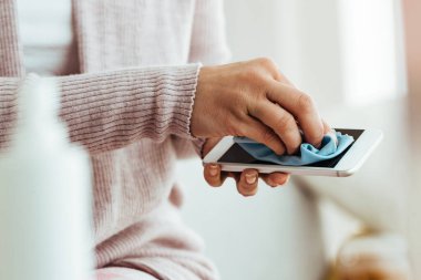 Close-up of woman using fabric cloth while cleaning her smart phone at home. 