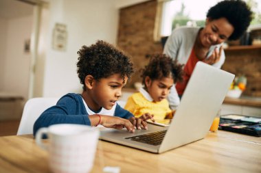 Smiling black boy surfing the net on a computer while being with his mother and sister at home. 