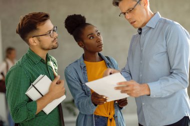 University professor talking to his students while standing in a hallway. Focus is on black female student. 