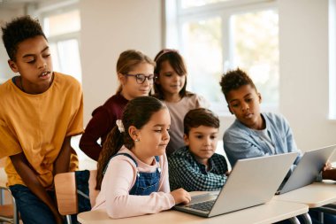 Group of elementary students e-learning while using laptop together in the classroom.
