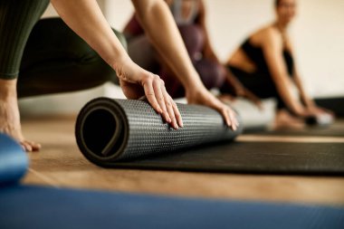 Close-up of athletic woman rolling up her exercise mat after practicing in health club. 