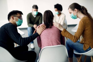 Supportive members of group therapy comforting one of the participants during coronavirus pandemic. 