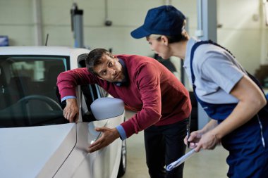 Mid adult man and female car mechanic communicating while analyzing vehicle breakdown in auto repair shop. 