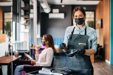 Hairstylist mixing hair dye and wearing face mask while working in a salon during COVID-19 pandemic.