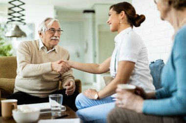 Happy mature man shaking hands with female nurse who is visiting him at home. 