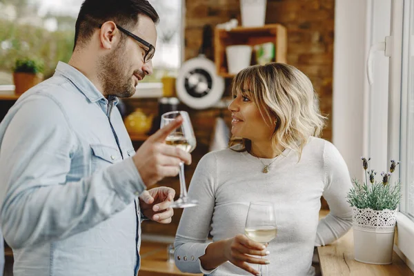 Happy couple communicating while drinking wine by the window in the kitchen. 
