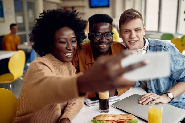 Multi-ethnic group of college students having fun while taking selfie with smart phone in cafeteria.
