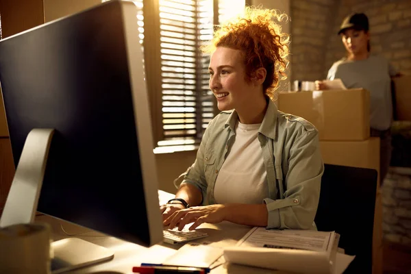 Young happy woman using computer while writing an e-mail and working in courier\'s office.