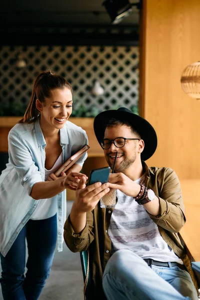 Happy university couple having fun while looking at something on smart phone in a cafe.