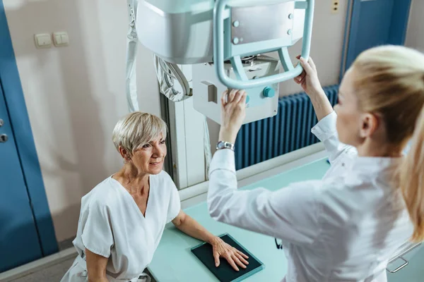 Mature female patient and medical technician during hand X-ray exam at clinic.