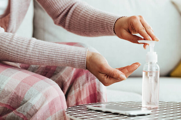 Close-up of woman using sanitizer gel dispenser while cleaning her hands at home. 