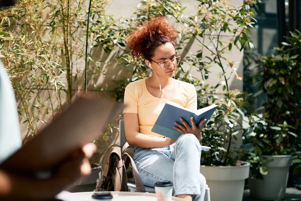 Female college student learning form a book while relaxing outdoors.