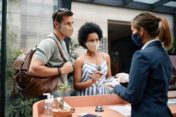 Happy Couple Wearing Face Masks While Talking Receptionist Signing Touchpad — Foto Stock