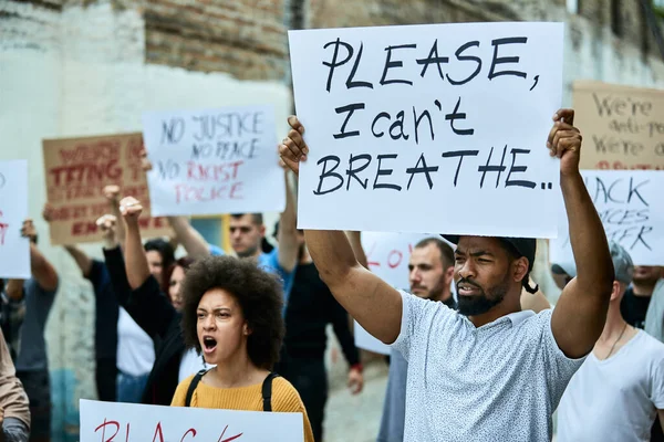 Large group of people on a Black Lives Matter protest. Focus is on black man holding a placard with Please, I can\'t breathe inscription.