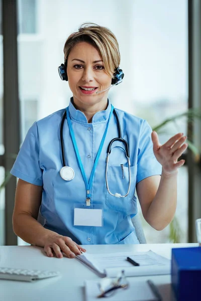 Smiling female doctor wearing headset and communicating with a patient while working at medical call center.