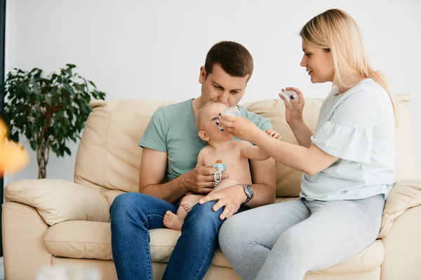 Young Father Holding Baby While Mother Feeding Him Bottle Home — Foto Stock