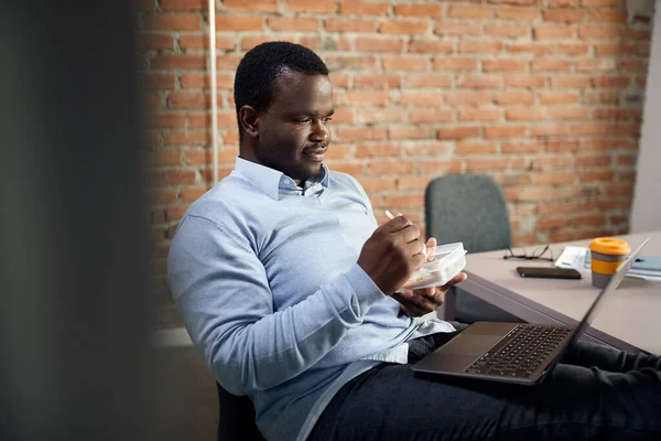 African American businessman surfing the net on laptop while having lunch break in the office.