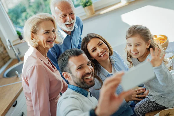 Happy multi-generation family using smart phone and having fun while taking selfie at home.