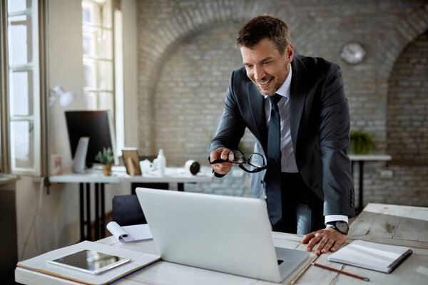 Happy mid adult businessman reading an e-mail on laptop while working in the office.