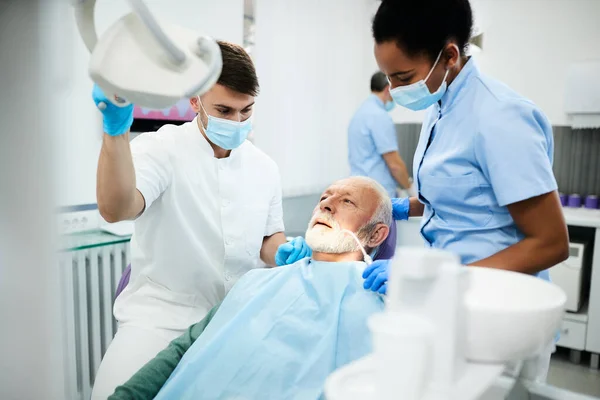 Young dentist and African American dental nurse with senior patient during dental examination at clinic.