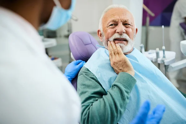Mature man talking about toothache problems with his dentist at dental clinic.