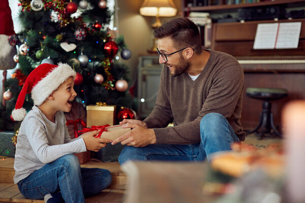 Счастливый отец дарит своему сыну подарок в рождественское утро дома.