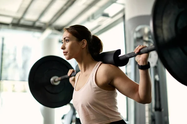 Determined female athlete having weight training and lifting barbell in a gym.