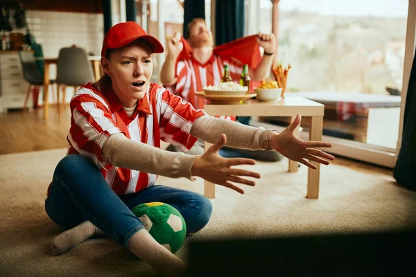 Displeased couple watching soccer match on Tv at home and feeling displeased after their favorite team has lost the match.