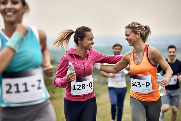 Happy athletic women supporting each other while running a marathon in nature.