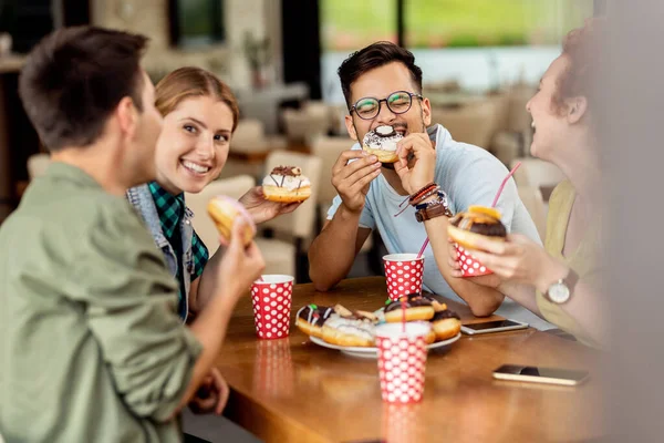 Group of happy friends eating donuts and having fun while communicating in a cafe.