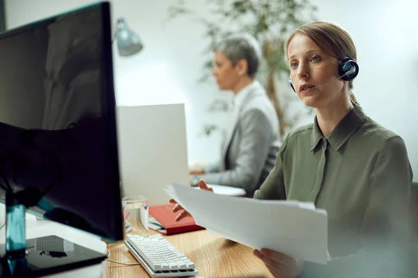 Female entrepreneur using computer and talking to someone via video call while working on business reports in the office.