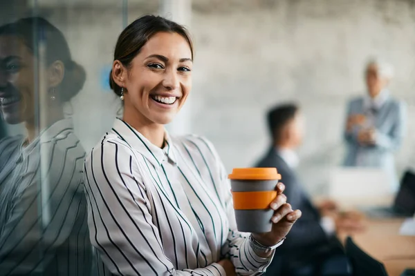 Happy female entrepreneur drinking coffee at corporate office and looking at camera.