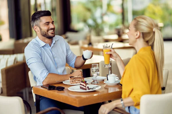 Happy man and his girlfriend communicating while having a drink during dessert in a cafe. 