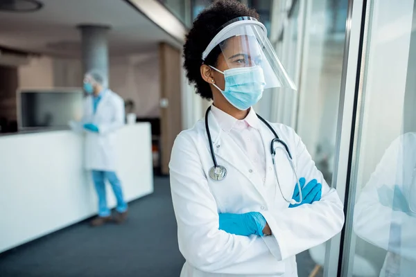 Pensive Black Female Doctor Looking Window While Wearing Face Shield — 스톡 사진