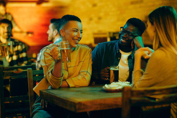 Happy friends enjoying in conversation and having fun while drinking beer at night in a bar. Focus is on African American woman. 