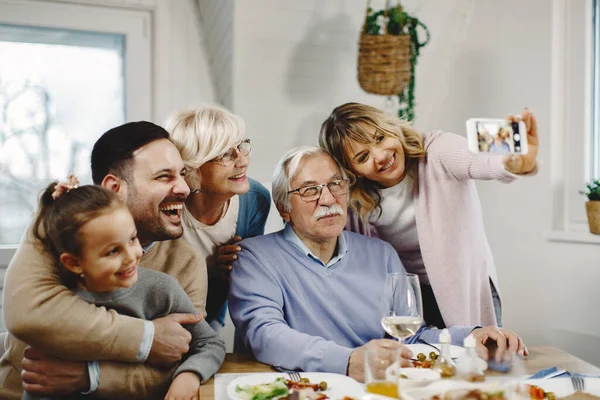 Cheerful extended family having fun while taking selfie with smart phone at dining table.