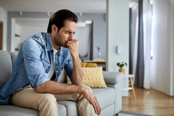 Young man feeling sad and sitting with eyes closed on the sofa.  