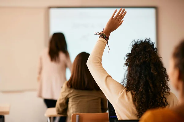 Back view of student raising her hand to answer a question during lecture at high school. 